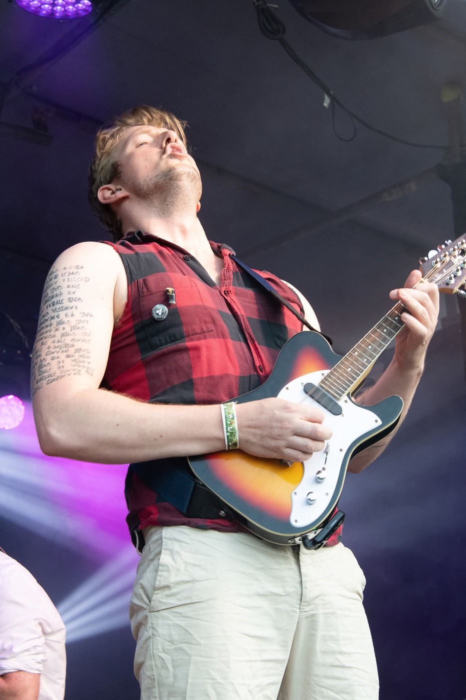 Gitarist in geruit hemd speelt met de ogen dicht op het podium van Turf Festival